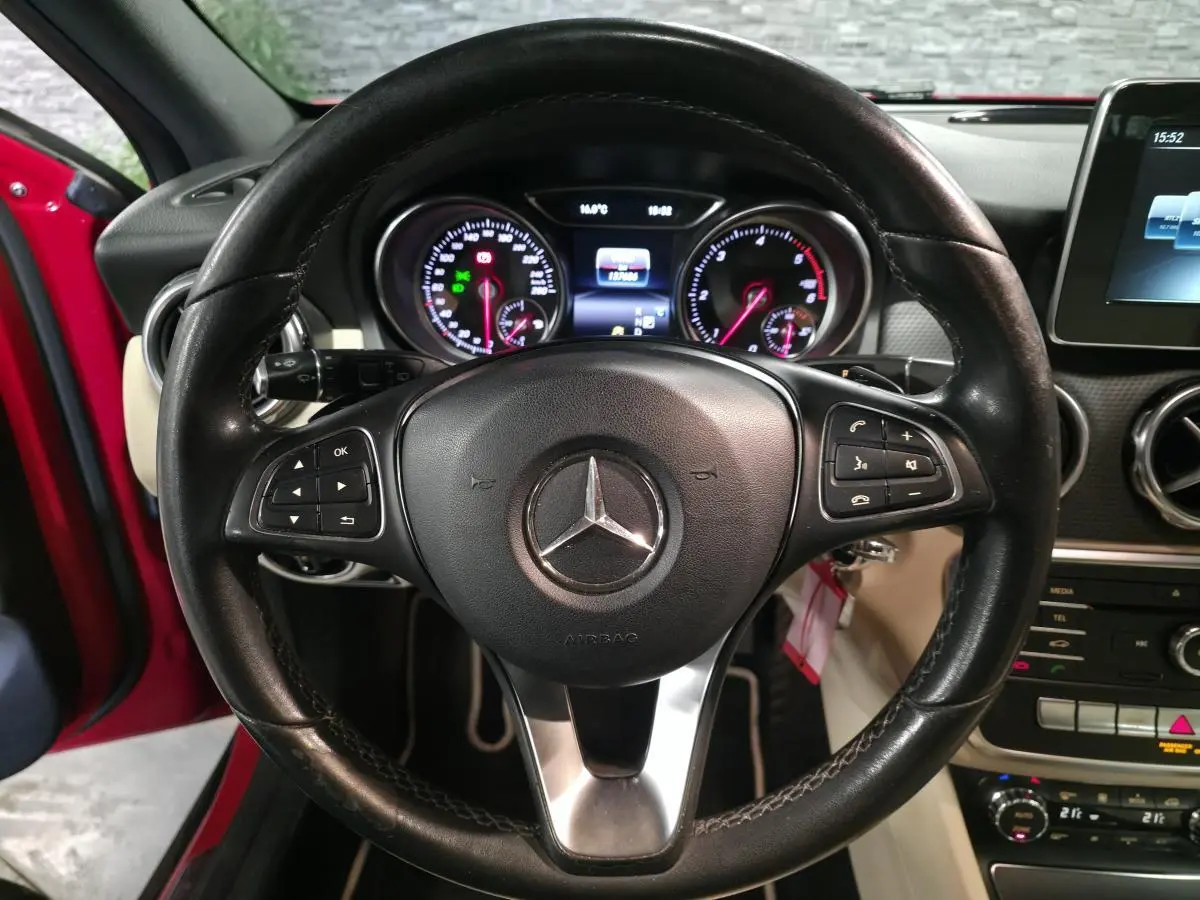 Vue centrée sur le volant cuir noir d'une Mercedes GLA rouge, avec tableau de bord et écran multimédia visibles.
