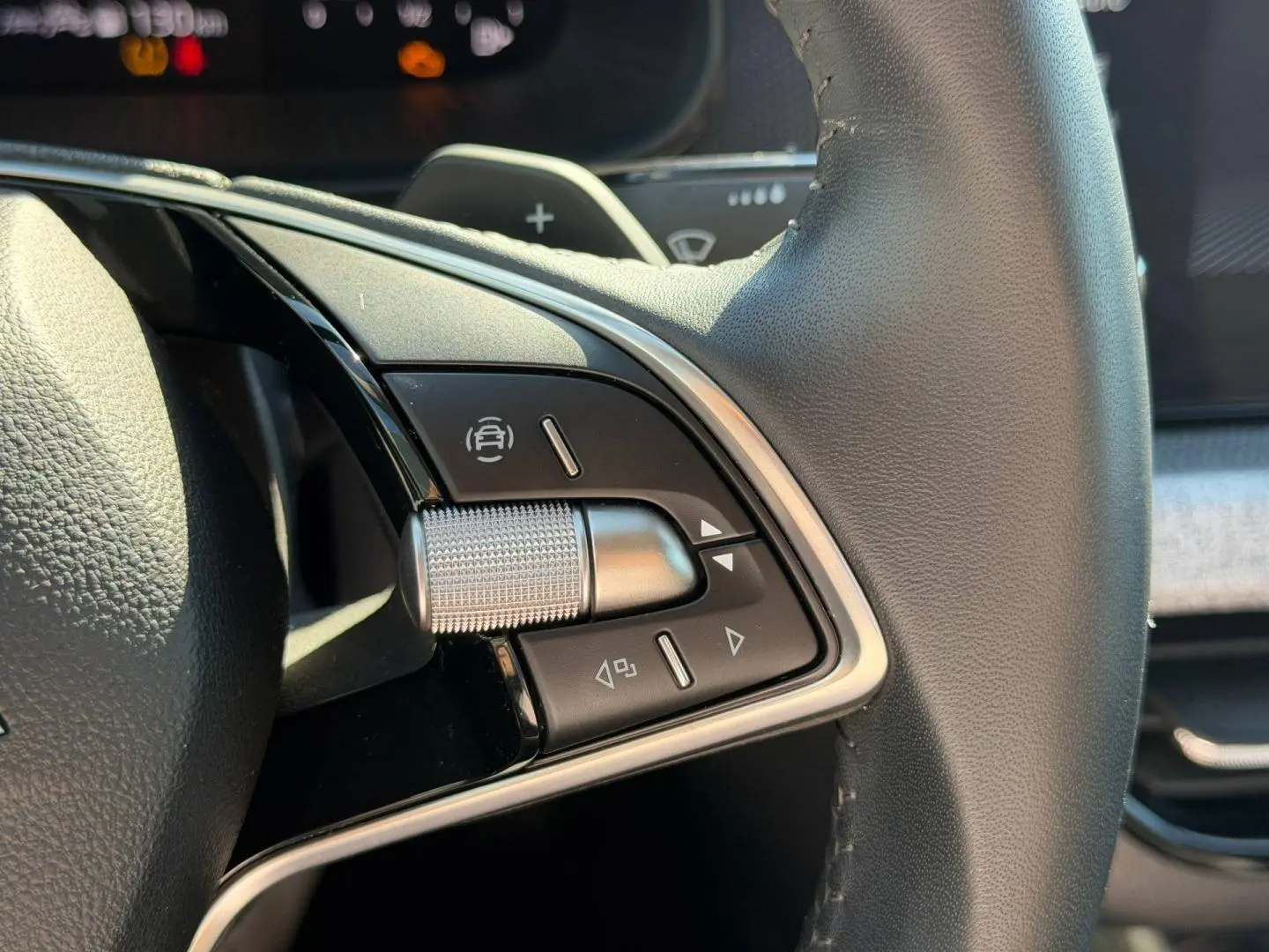Gros plan sur les commandes gauche du volant cuir noir du Skoda Scala gris, avec molette et boutons multifonctions.