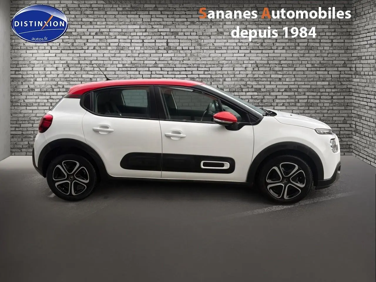 Profil latéral gauche d'une Citroën C3 2021 blanche avec toit et rétroviseurs rouges, enjoliveurs noirs distinctifs.