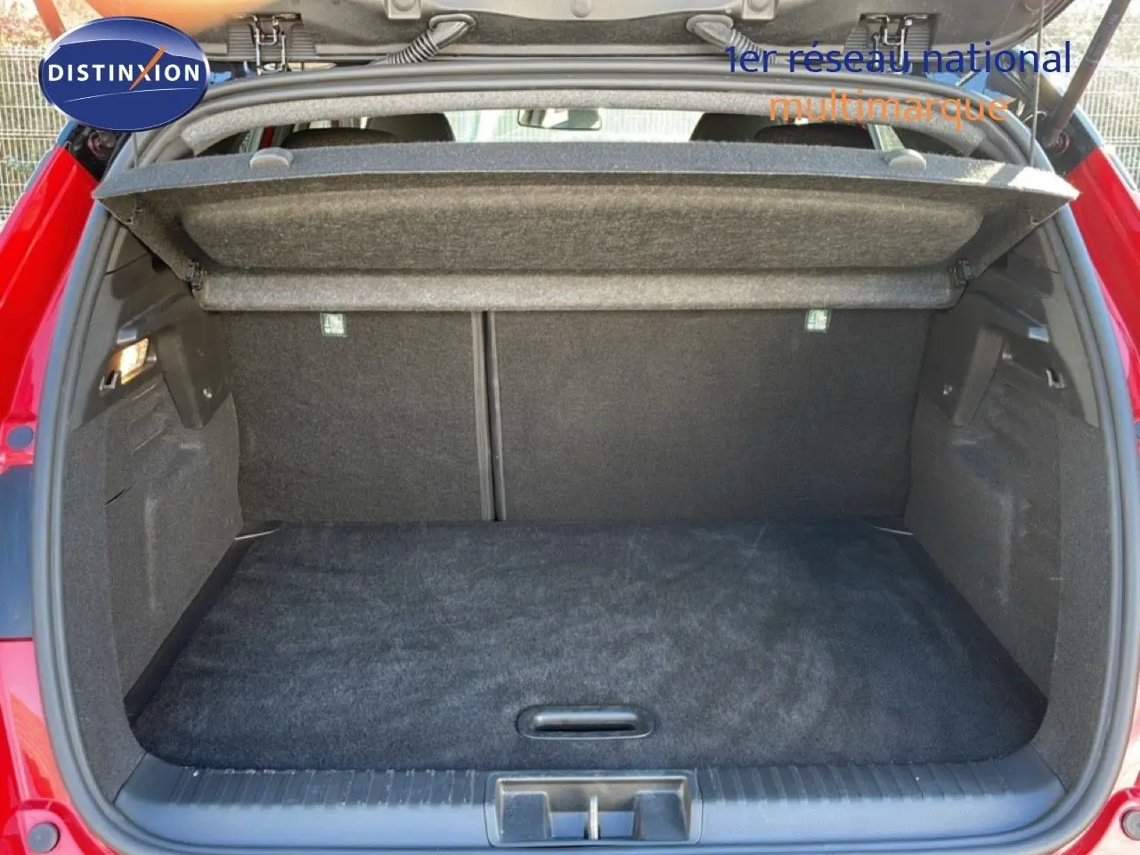 Coffre ouvert vu de l'arrière d'un Renault Captur rouge Désir Métal avec toit noir, espace de chargement vide et tapis noir.