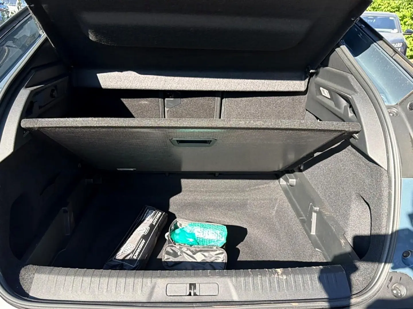Coffre ouvert d’un Peugeot 3008 bleu Ingara, montrant le plancher de coffre mobile et un kit de sécurité.