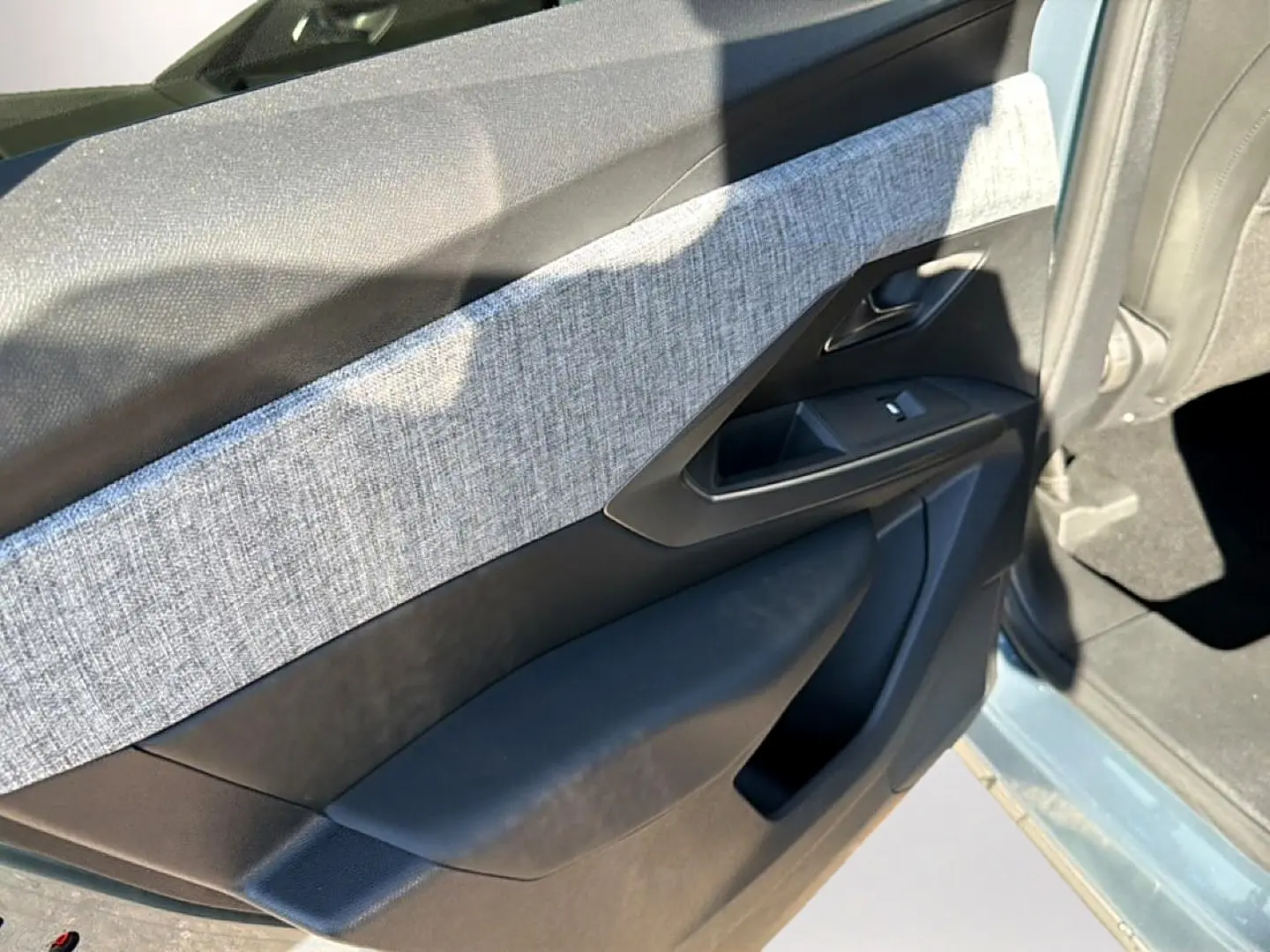 Vue intérieure du panneau de porte avant gauche du Peugeot 3008 bleu Ingara avec habillage tissu gris et commandes de vitre.