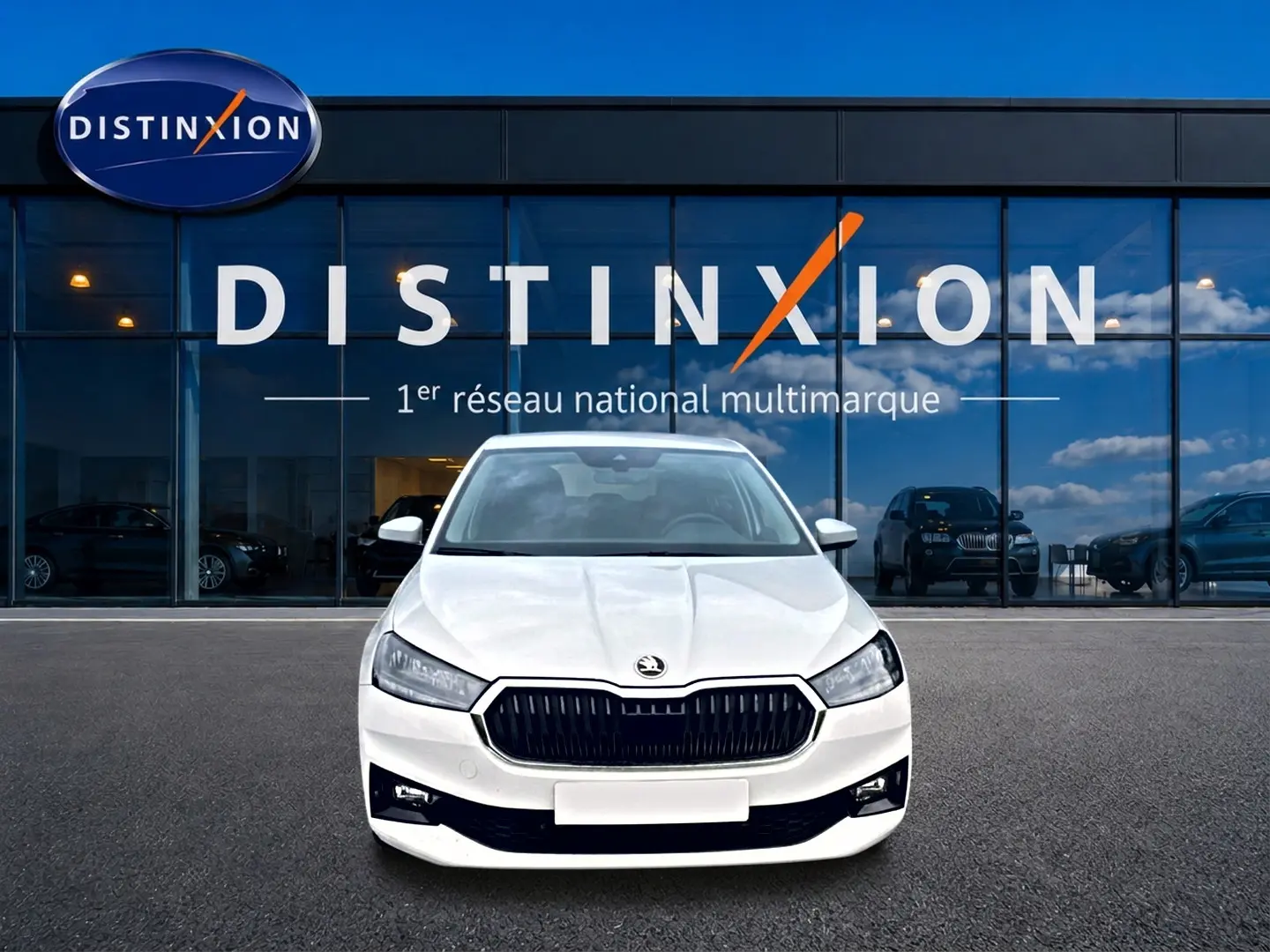 Vue frontale d'une Skoda Fabia blanche 2025 garée devant une vitrine avec logo Distinxion.