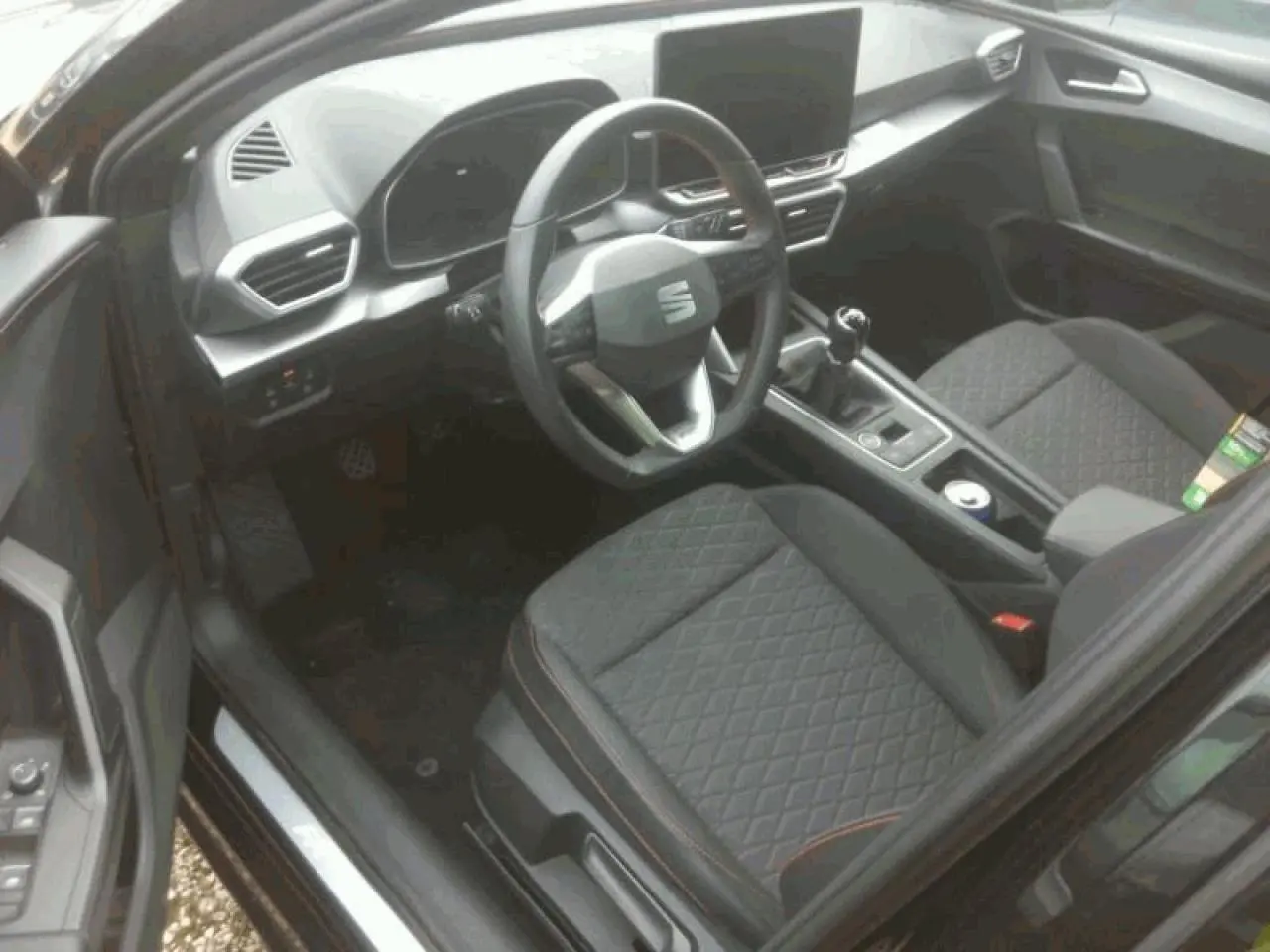 Vue intérieure côté conducteur du SEAT LEON ST 2025, volant multifonction cuir et sièges sport noirs avec surpiqûres rouges.