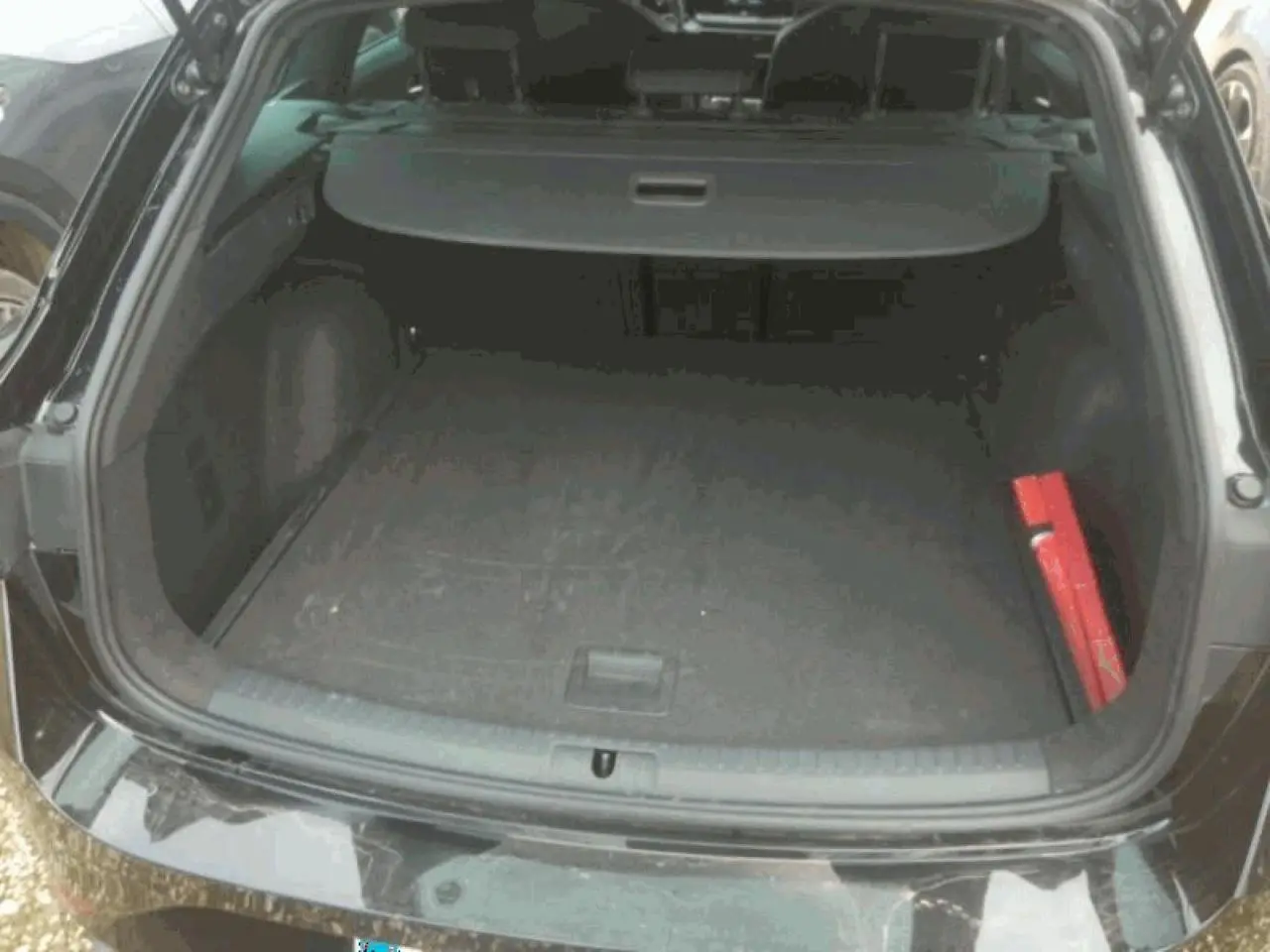 Coffre ouvert vu de l'arrière d'une SEAT LEON ST noir minuit, avec cache-bagages et kit de sécurité rouge visible.