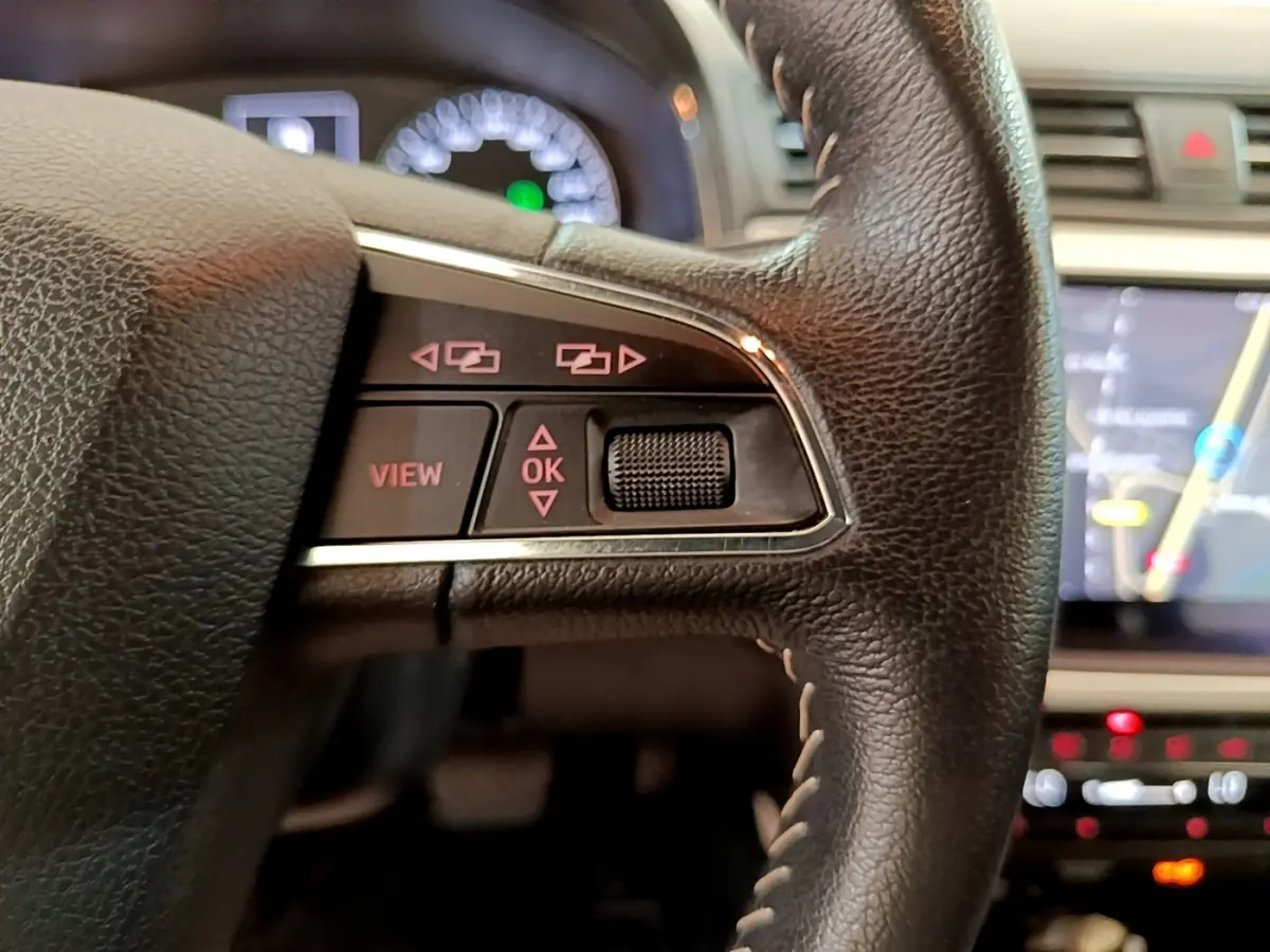 Gros plan sur le côté gauche du volant cuir et alu du SEAT Arona 2019 avec commandes multifonctions et écran tactile en arrière-plan.