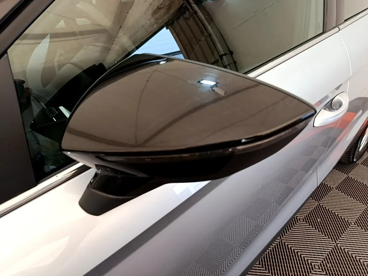 Gros plan sur le rétroviseur droit noir brillant d'une SEAT Arona gris clair, avec partie latérale et poignée de porte visibles.