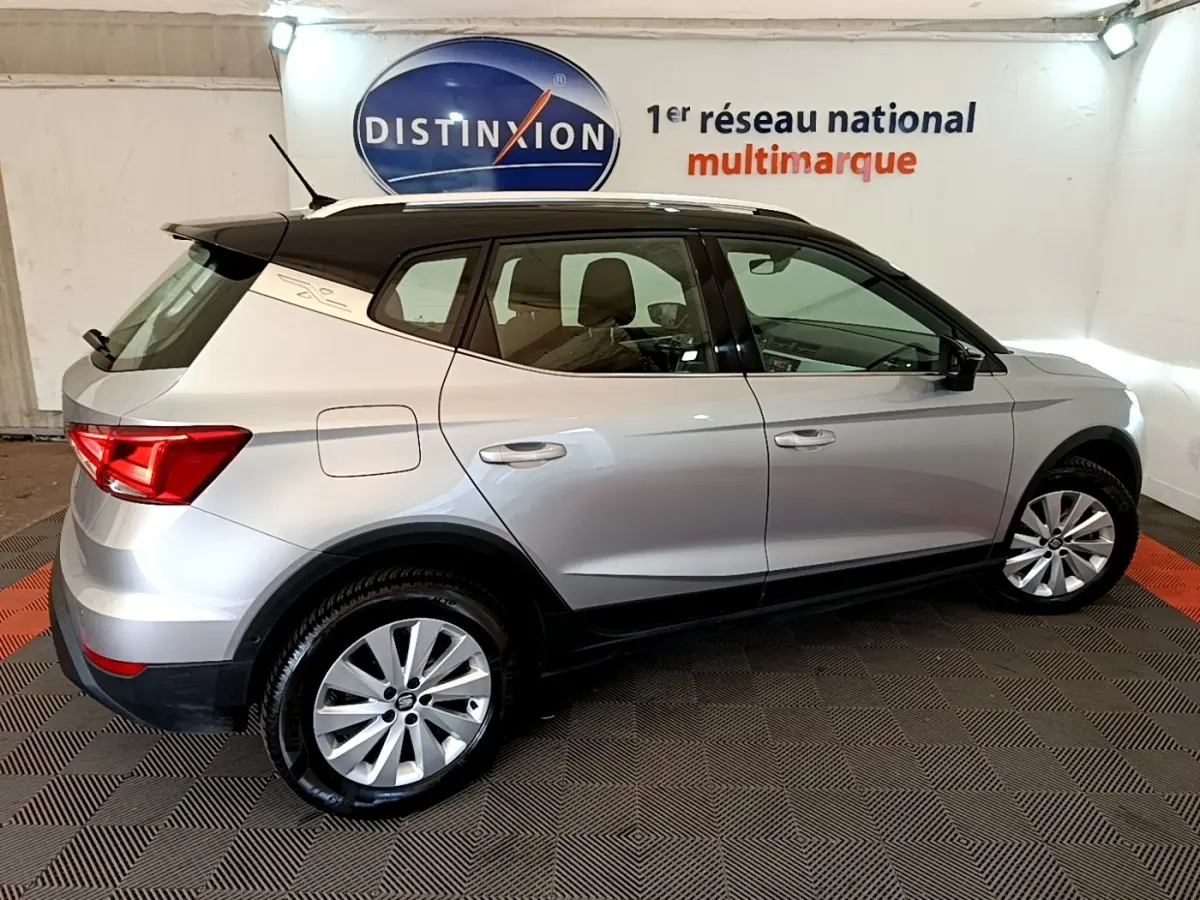 Vue de profil côté droit d'un SEAT Arona gris clair avec toit noir et jantes alliage dans un showroom.