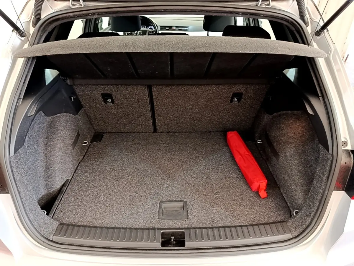 Coffre ouvert d’une SEAT Arona gris clair, vue arrière, avec tapis gris et un objet rouge posé à droite.