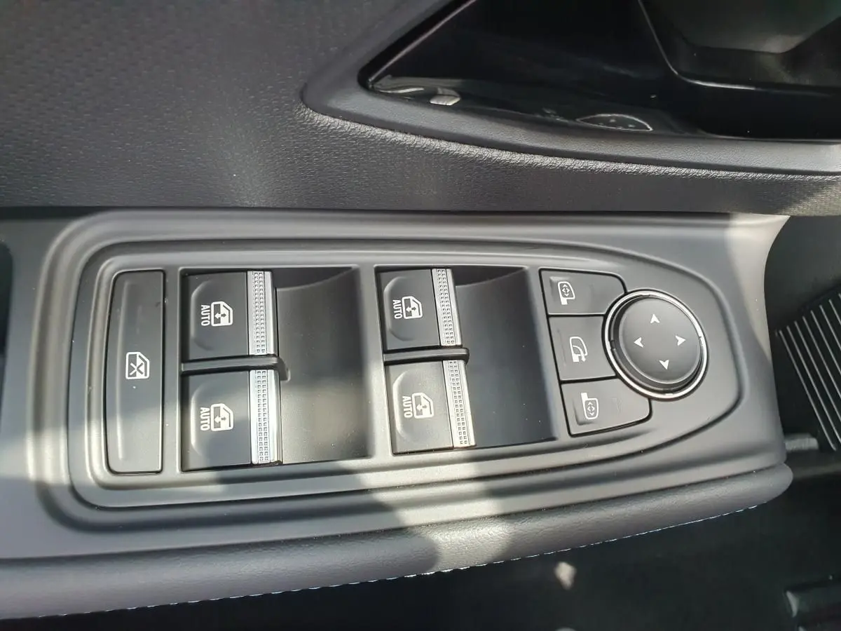 Gros plan sur les commandes des vitres électriques et réglages des rétroviseurs côté conducteur d'une Renault Clio VI gris Rafale.