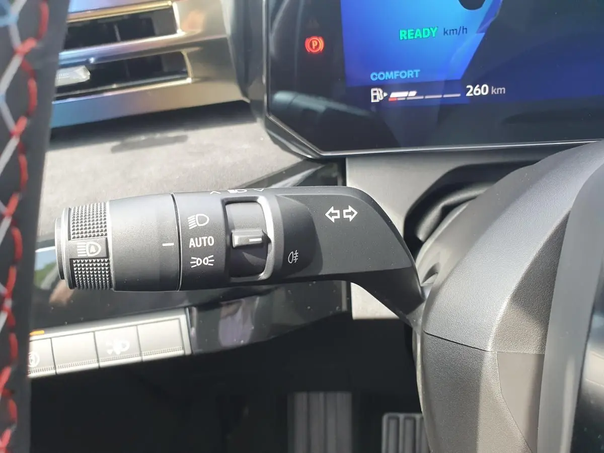 Gros plan sur la commande des feux et clignotants à gauche du volant dans le tableau de bord gris de la Renault Clio VI hybride.