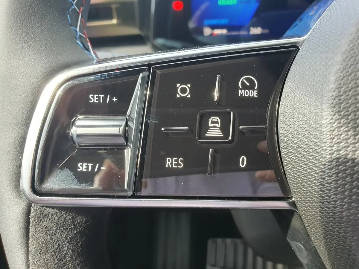 Gros plan sur les commandes au volant côté gauche de la Renault Clio VI hybride, finition Esprit Alpine, avec boutons de régulateur et mode conduite.