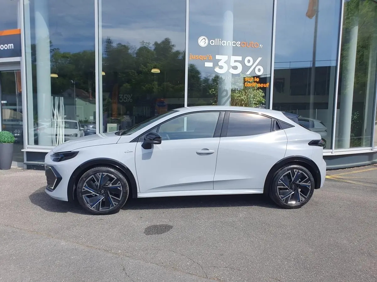 Profil droit de la Renault Clio VI gris Rafale 2026 avec jantes alliage 18” et vitres teintées, devant une vitrine.