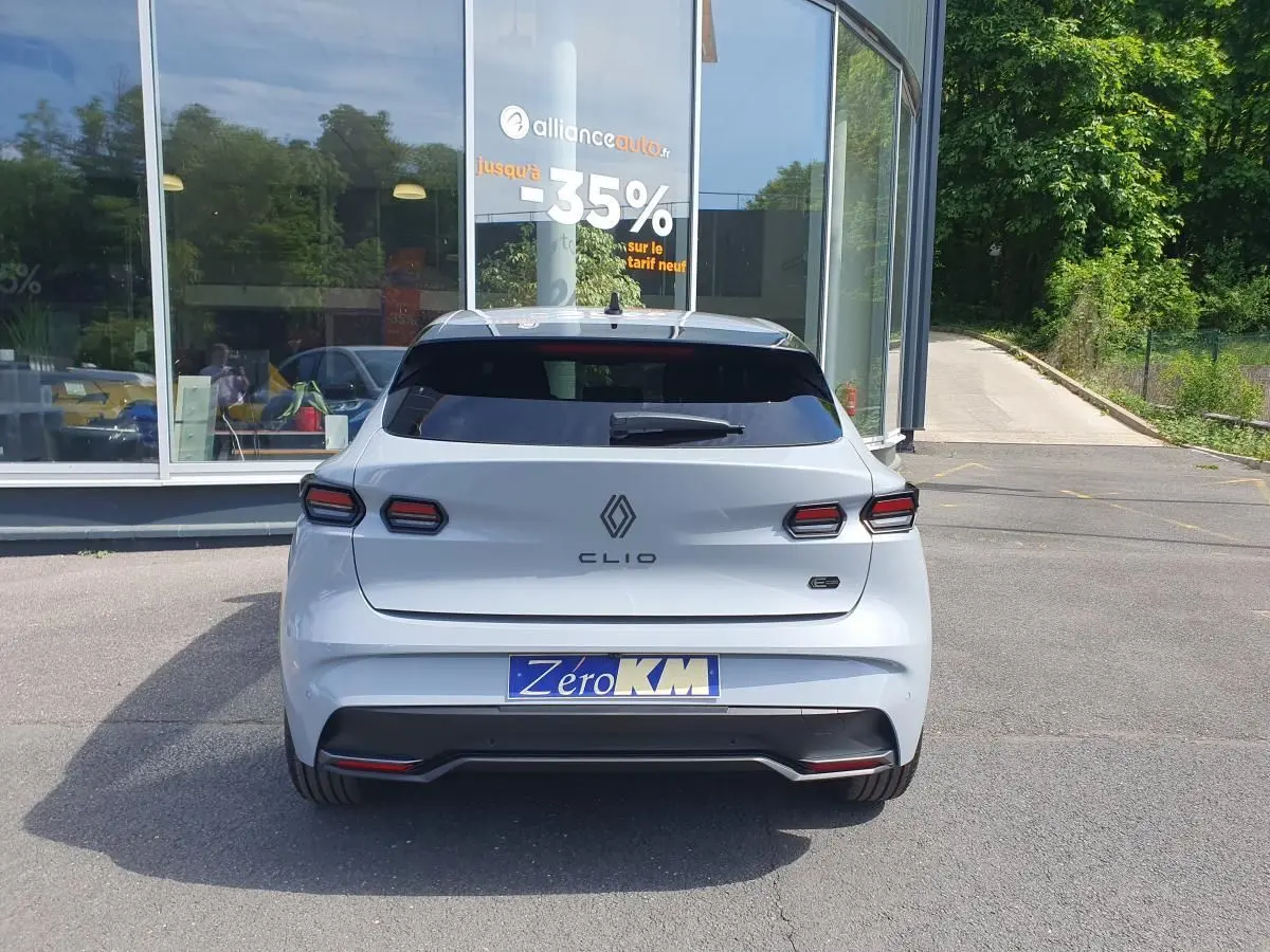 Vue arrière d'une Renault Clio VI gris Rafale avec feux LED et logo distinctif, stationnée devant un bâtiment vitré.