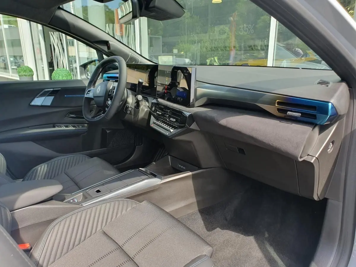 Vue intérieure côté conducteur de la Renault Clio VI hybride 2026, tableau de bord moderne et sièges gris raffinés.