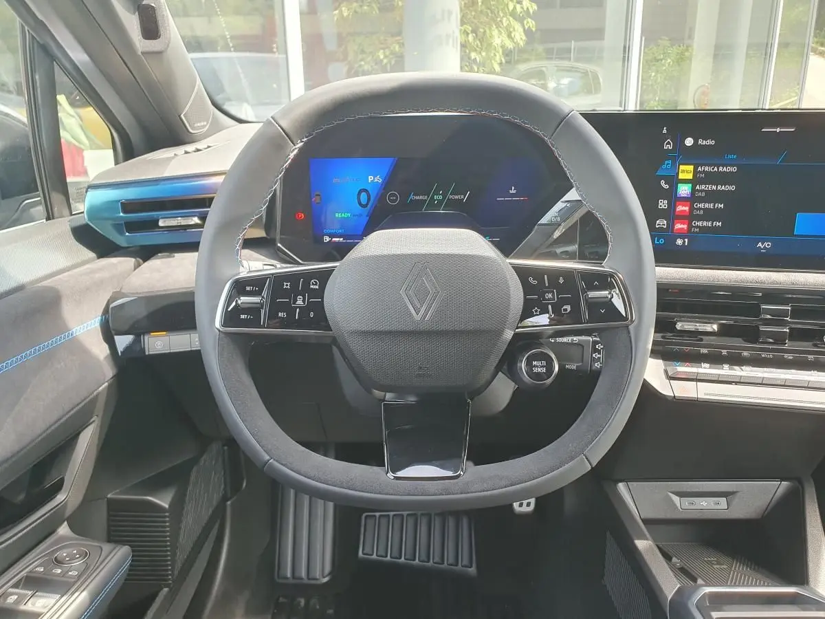 Vue intérieure centrée sur le volant noir avec logo Renault, tableau de bord numérique et écran tactile à droite.