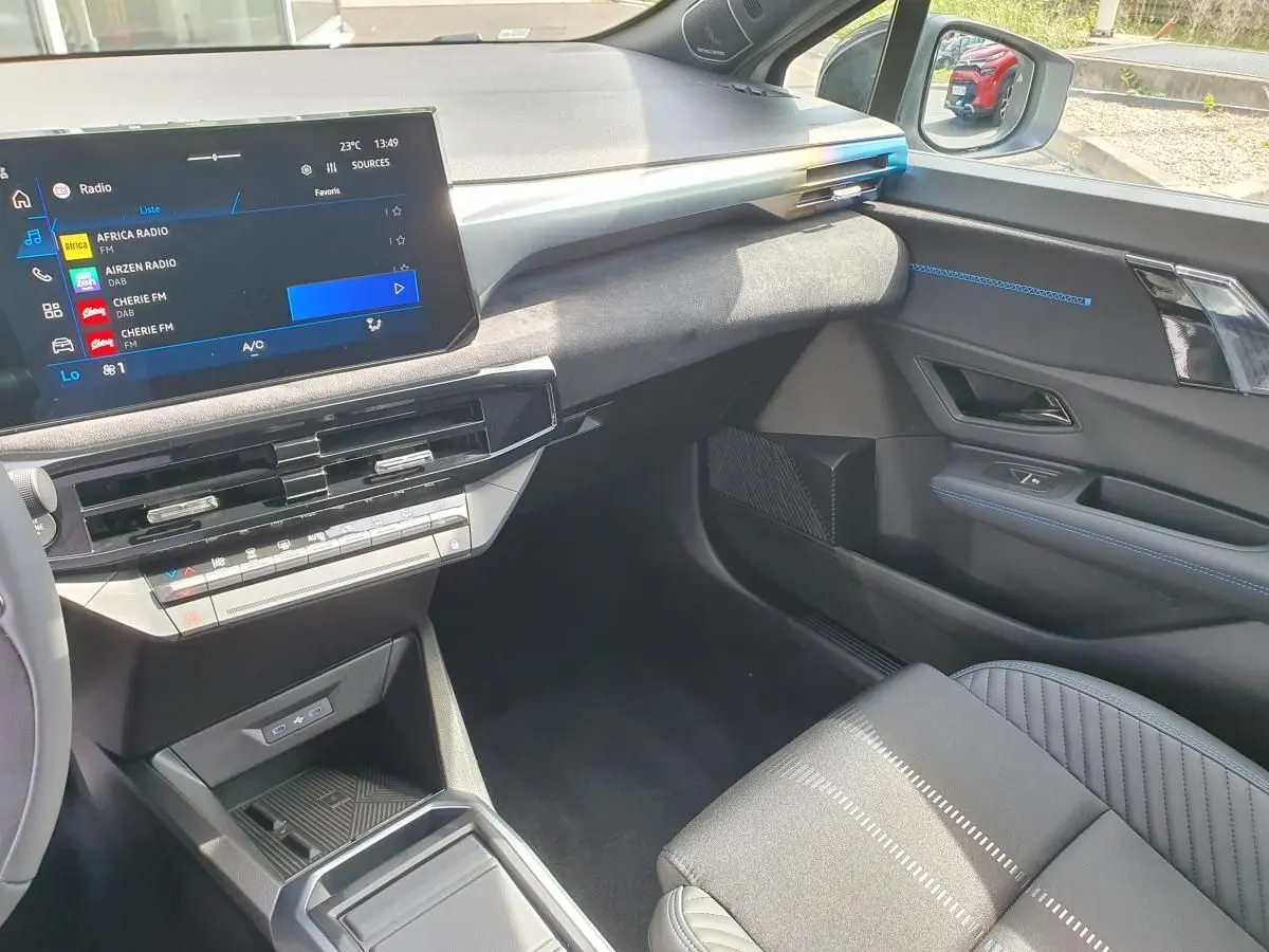 Vue intérieure côté passager de la Renault Clio VI gris Rafale, avec écran tactile et finitions bleues sur la porte.