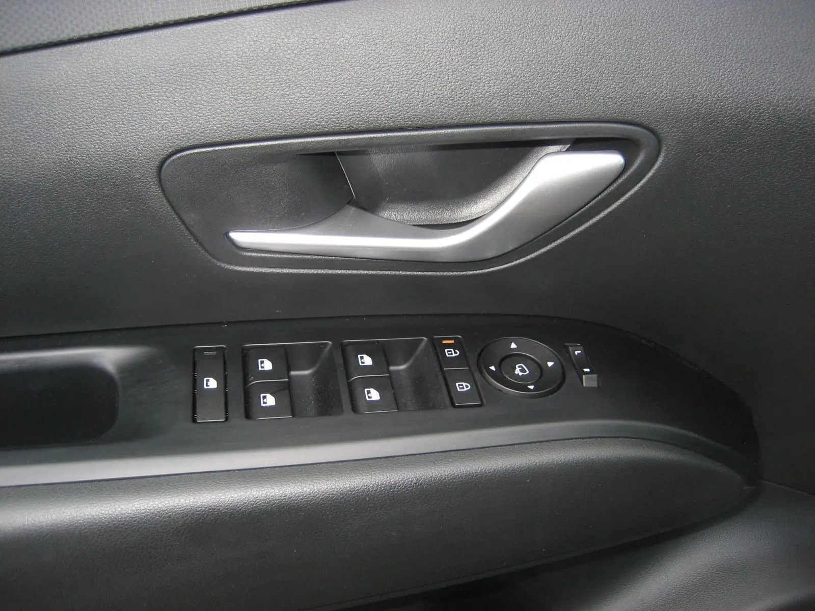 Gros plan sur la poignée de porte intérieure et les commandes des vitres du côté conducteur d'un Hyundai Tucson gris Ecotronic 2025.