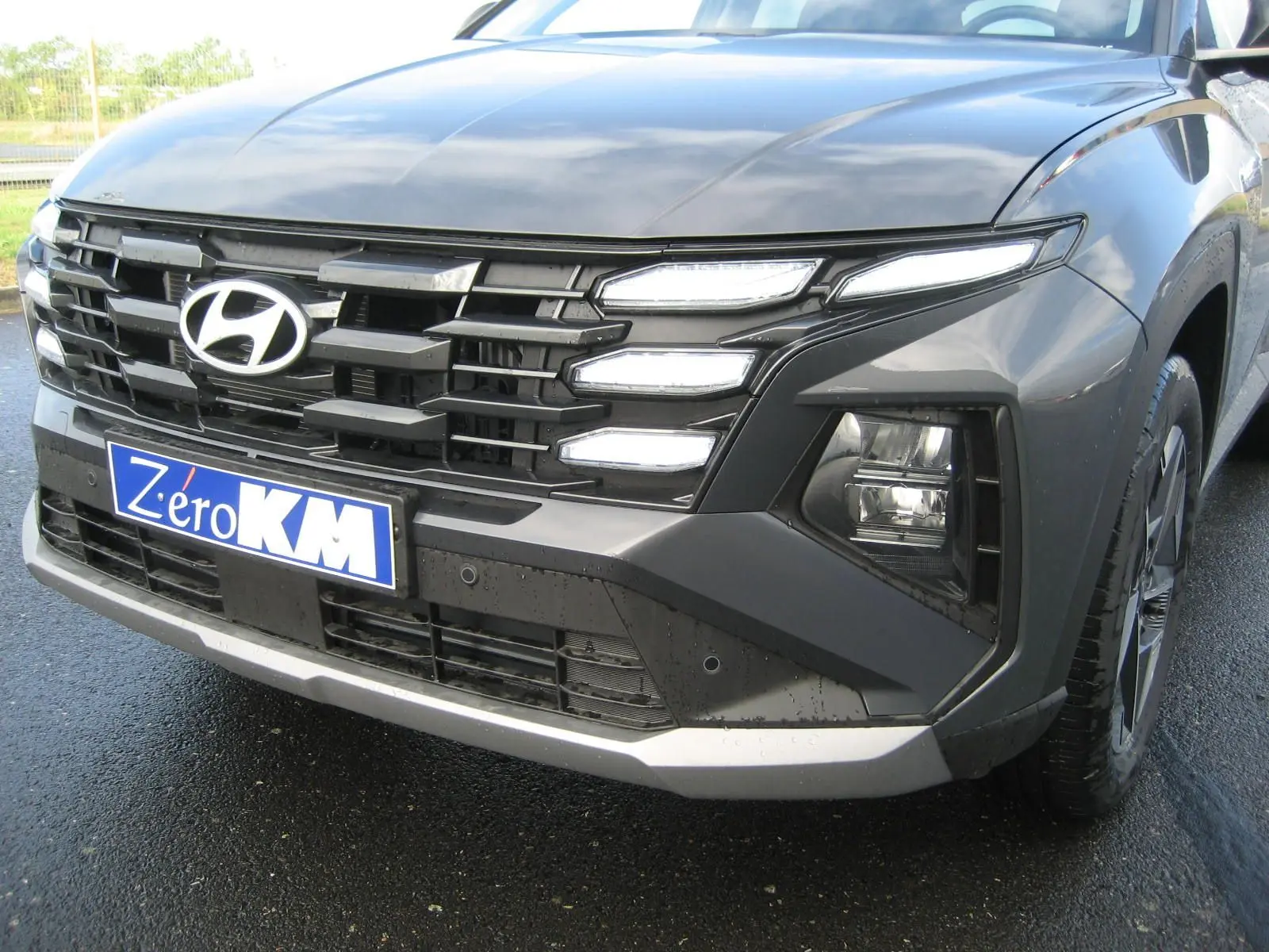 Vue de face droite du Hyundai Tucson 2025 gris Ecotronic avec calandre imposante et feux LED distinctifs allumés.