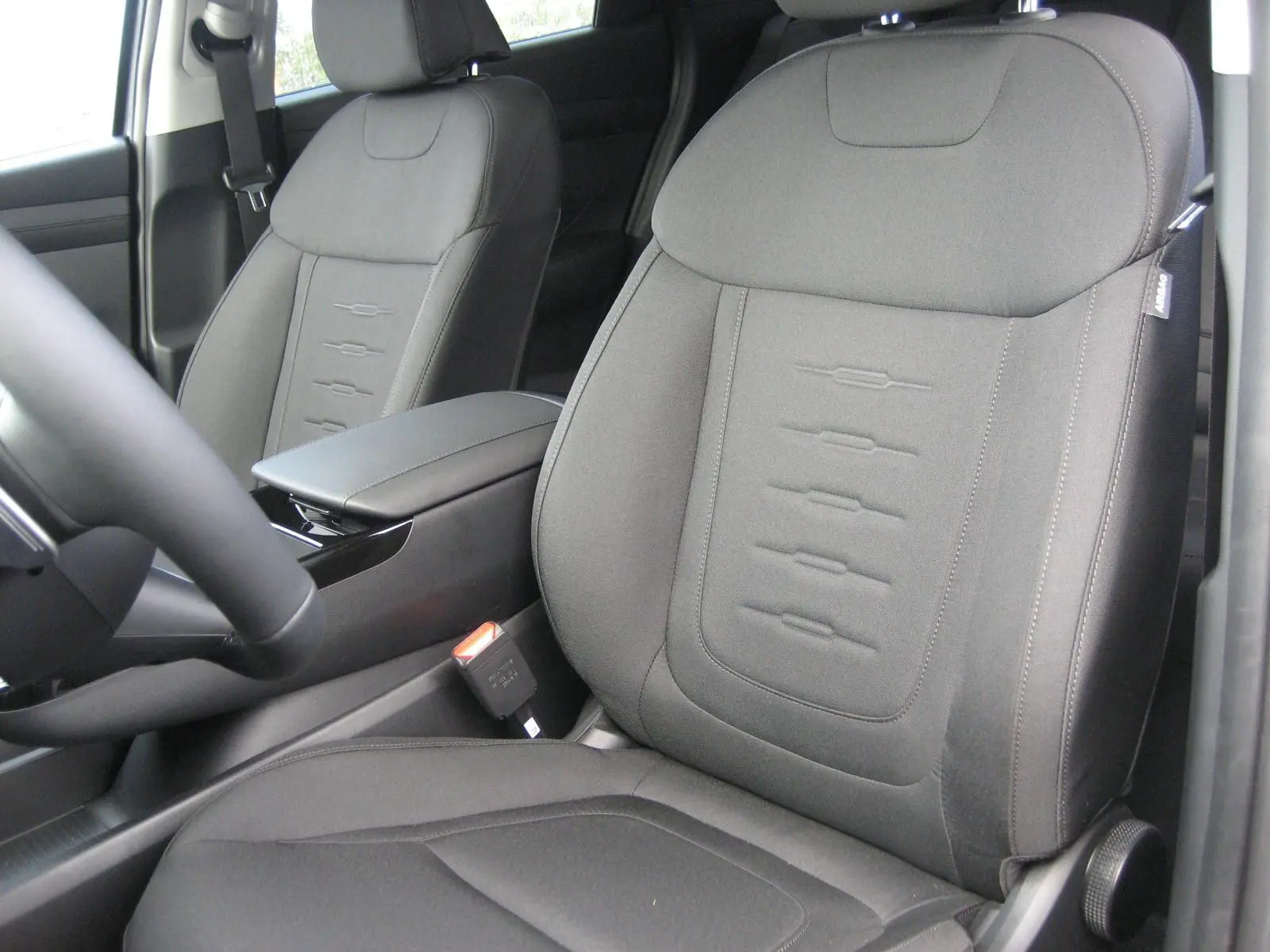 Gros plan sur les sièges avant gris foncé du Hyundai Tucson 2025, avec accoudoir central et ceinture de sécurité visible.
