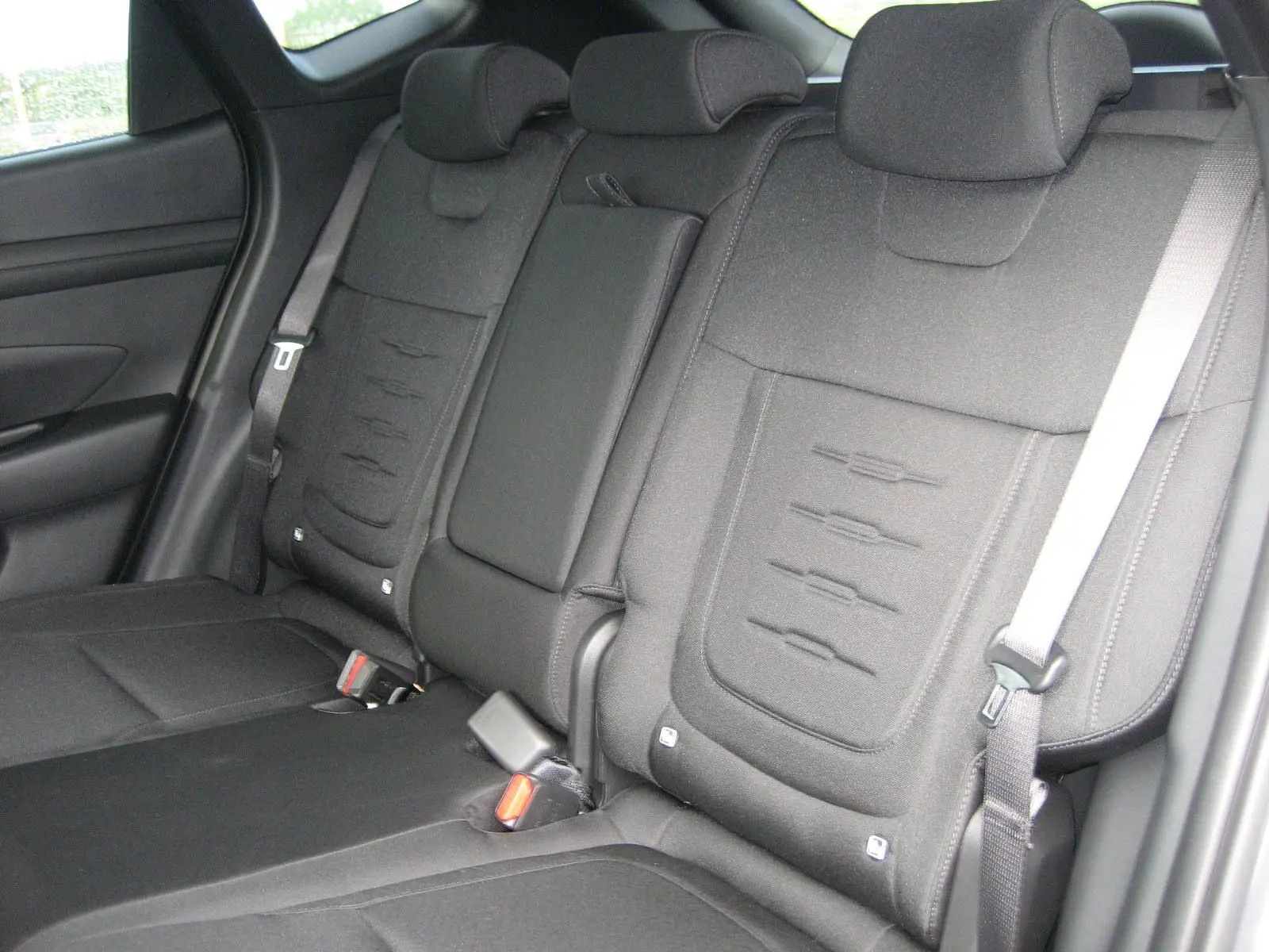 Vue intérieure des sièges arrière noirs du Hyundai Tucson IV PH.2 Style 1.6 T-GDI Hybrid 215, avec appuie-têtes et ceintures visibles.