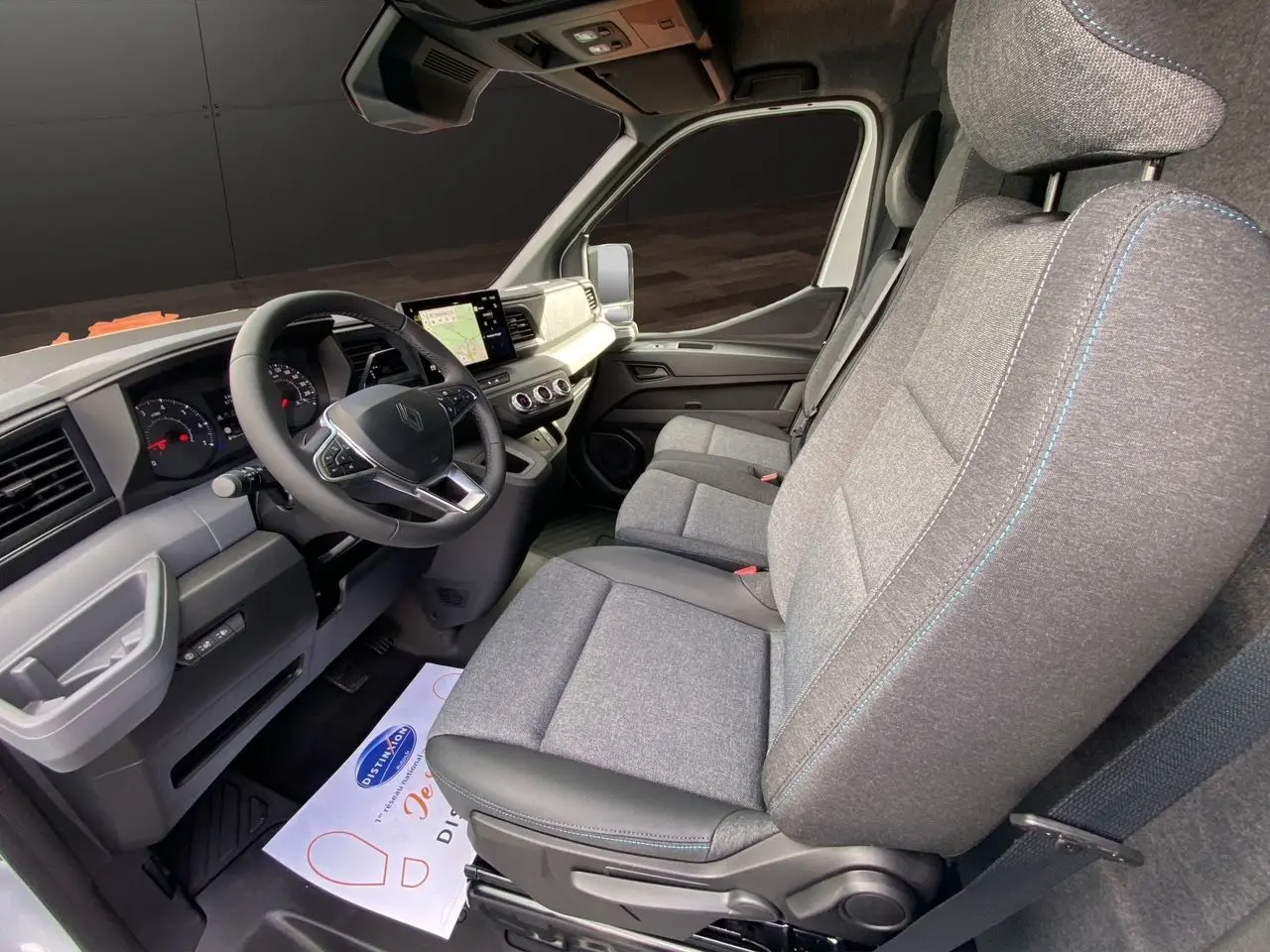 Vue intérieure côté conducteur du Renault Master 2025, sièges gris avec surpiqûres bleues et tableau de bord moderne noir et gris.