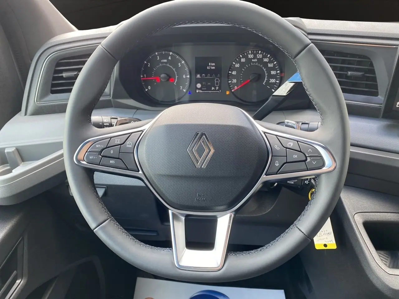 Vue rapprochée du volant noir du Renault Master 2025 avec commandes intégrées et tableau de bord numérique en arrière-plan.