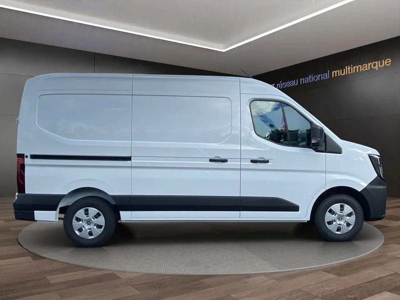 Vue de profil côté droit du Renault Master blanc 2025 avec bande noire et jantes argentées, dans un showroom intérieur.