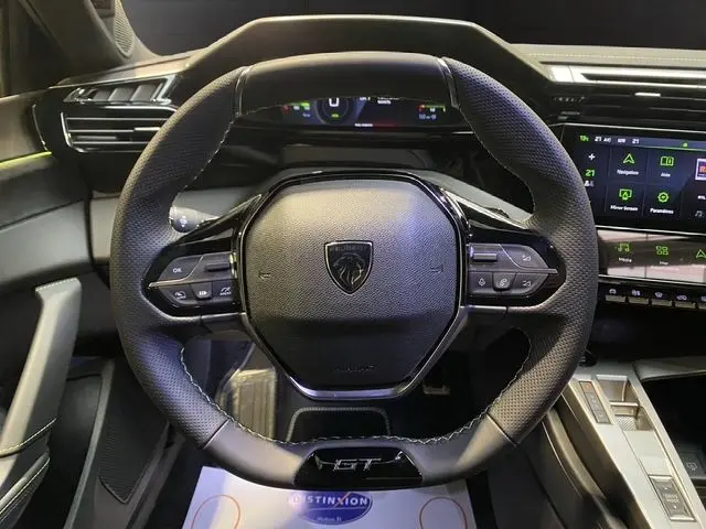 Vue rapprochée du volant cuir noir GT de la Peugeot 308 Hybrid 2026 avec tableau de bord digital et écran tactile.