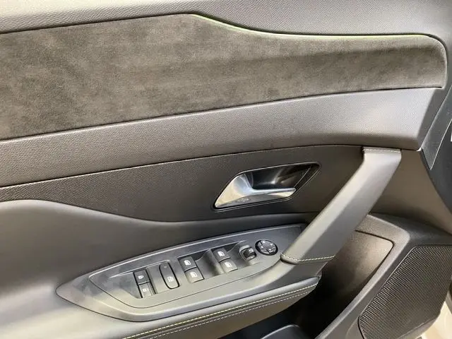 Détail de la porte intérieure côté conducteur en cuir noir avec commandes électriques et poignée argentée.