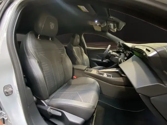 Vue intérieure côté conducteur de la Peugeot 308 blanche, sièges en cuir noir avec logo Peugeot brodé sur les appuie-têtes.