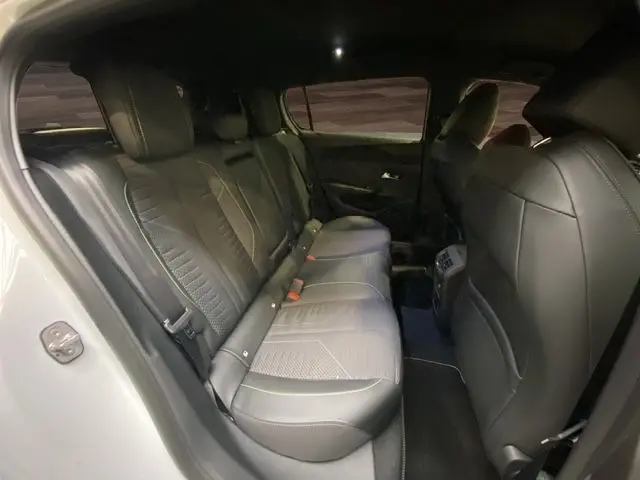 Vue intérieure arrière gauche de la Peugeot 308 hybride blanche, sièges en cuir noir avec surpiqûres et ceintures visibles.