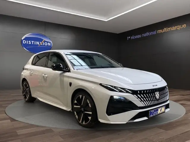 Peugeot 308 hybride blanche vue 3/4 avant droit, avec calandre distinctive et jantes noires bicolores.