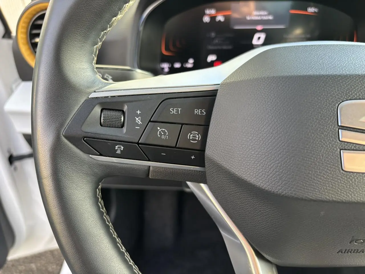Gros plan sur le volant noir du SEAT Arona blanc, mettant en valeur les commandes de régulateur de vitesse à gauche.