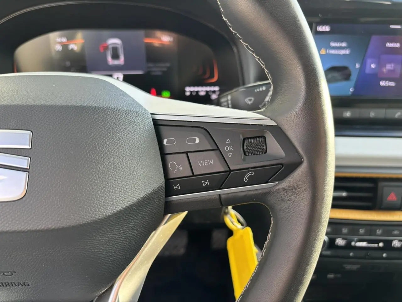 Gros plan sur le volant côté droit du SEAT Arona blanc 2025 avec commandes multimédia et tableau de bord digital flou.