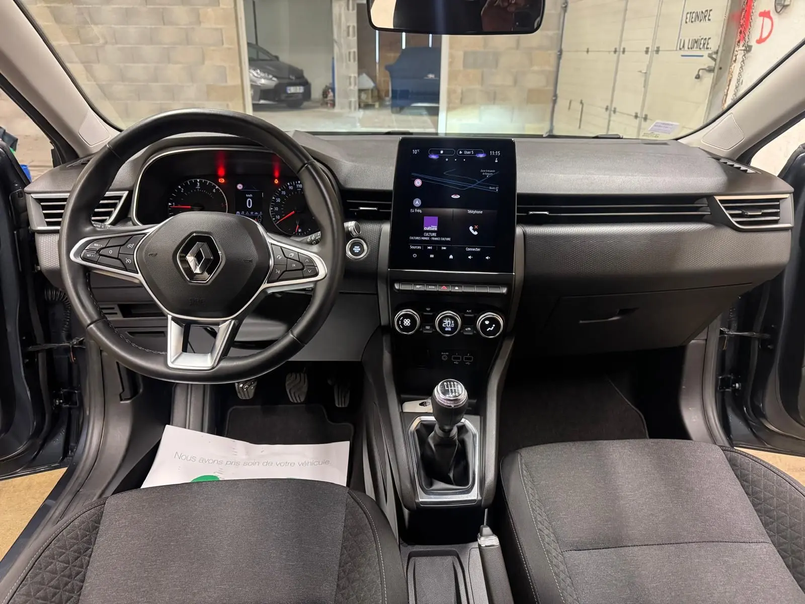 Vue intérieure avant de la Renault Clio V Business 2019, avec tableau de bord noir, écran tactile vertical et levier de vitesses manuel.