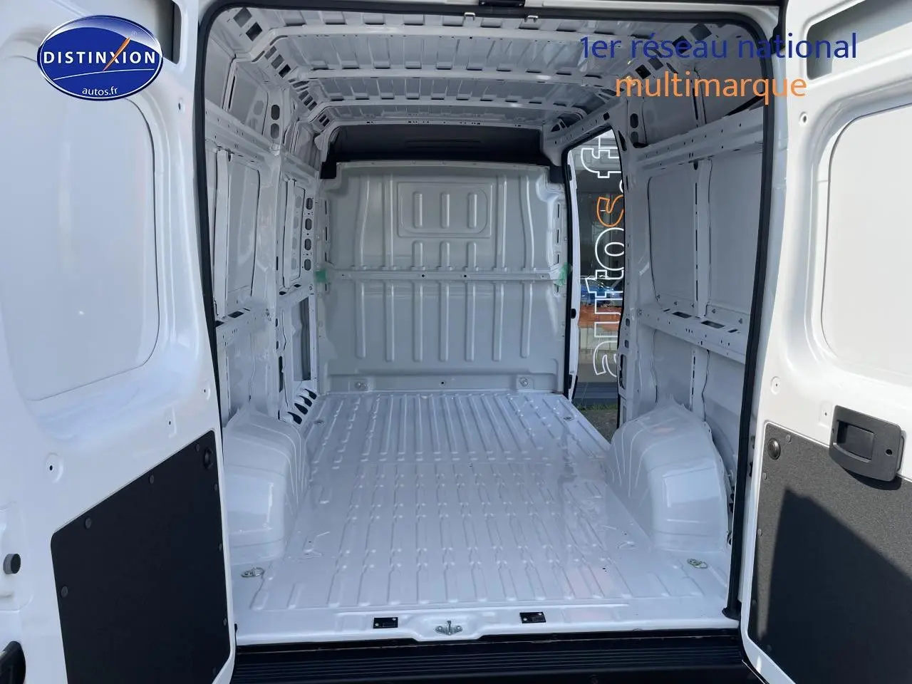Intérieur du fourgon Peugeot Boxer blanc vu de l’arrière, montrant l’espace de chargement vide et la porte ouverte.