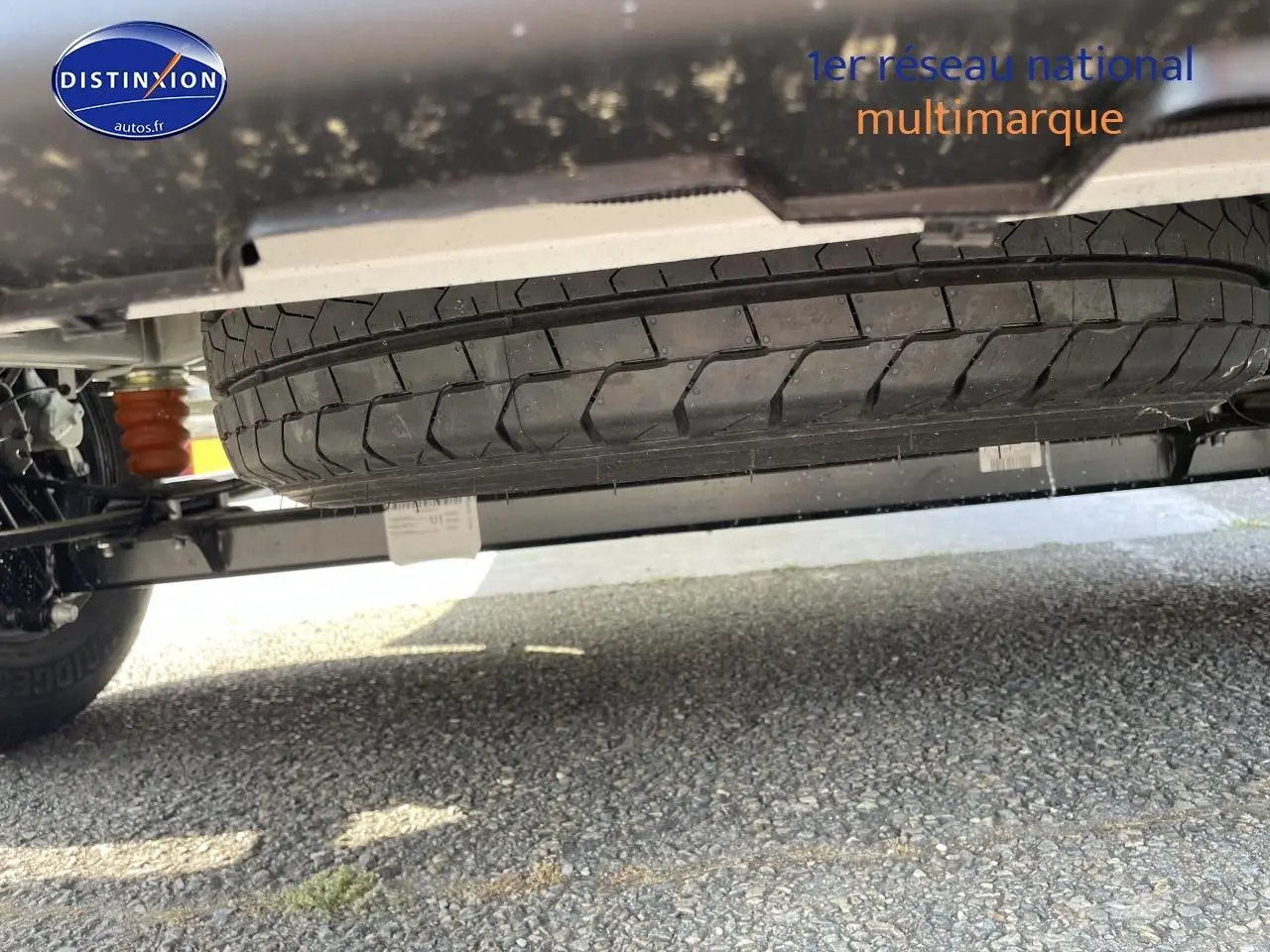 Vue en contre-plongée sous un Peugeot Boxer Fourgon blanc, mettant en valeur la roue de secours et le châssis.