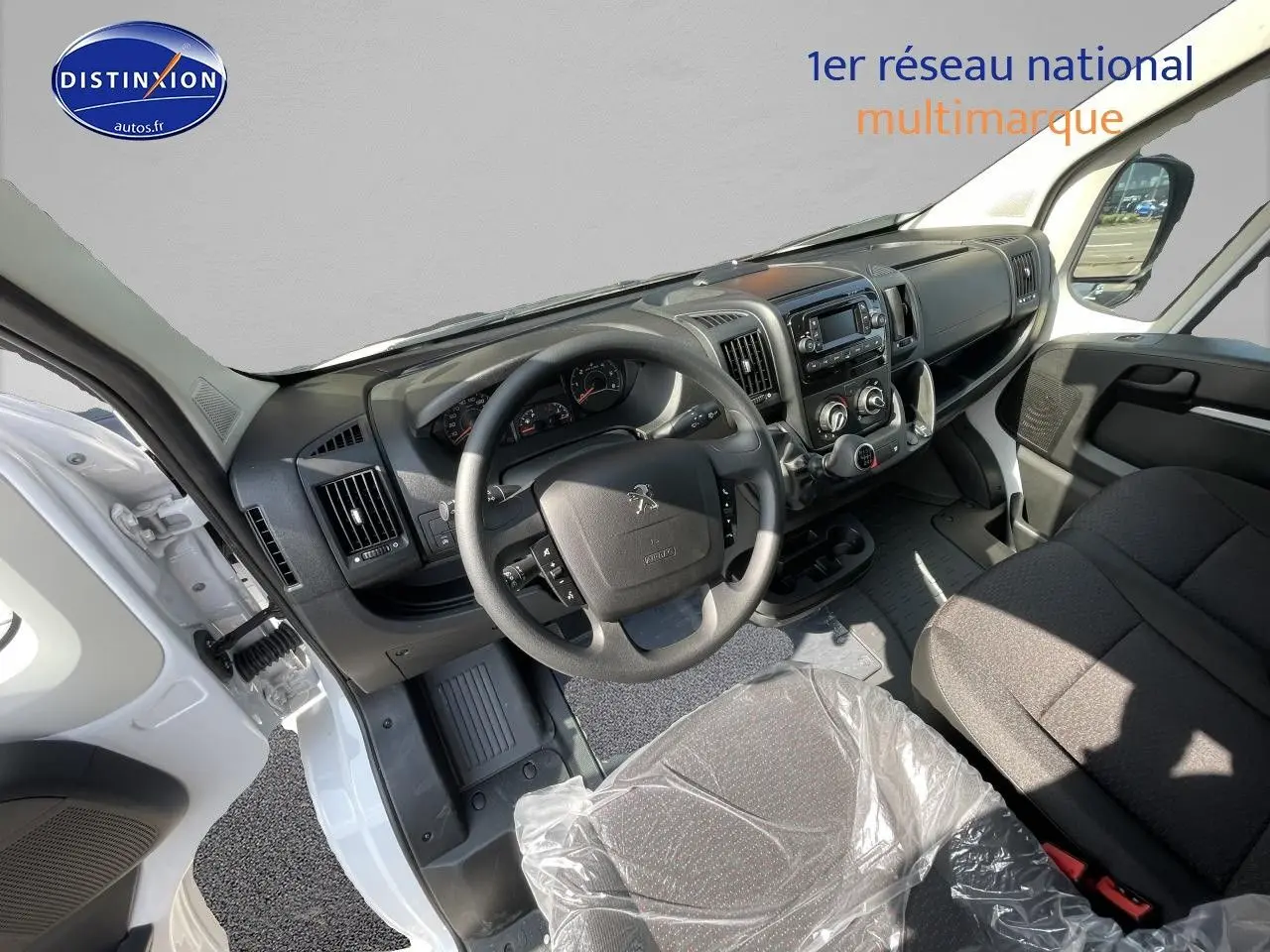 Vue intérieure côté conducteur du Peugeot Boxer Fourgon blanc 2023, tableau de bord et volant visibles, siège protégé par une housse plastique.