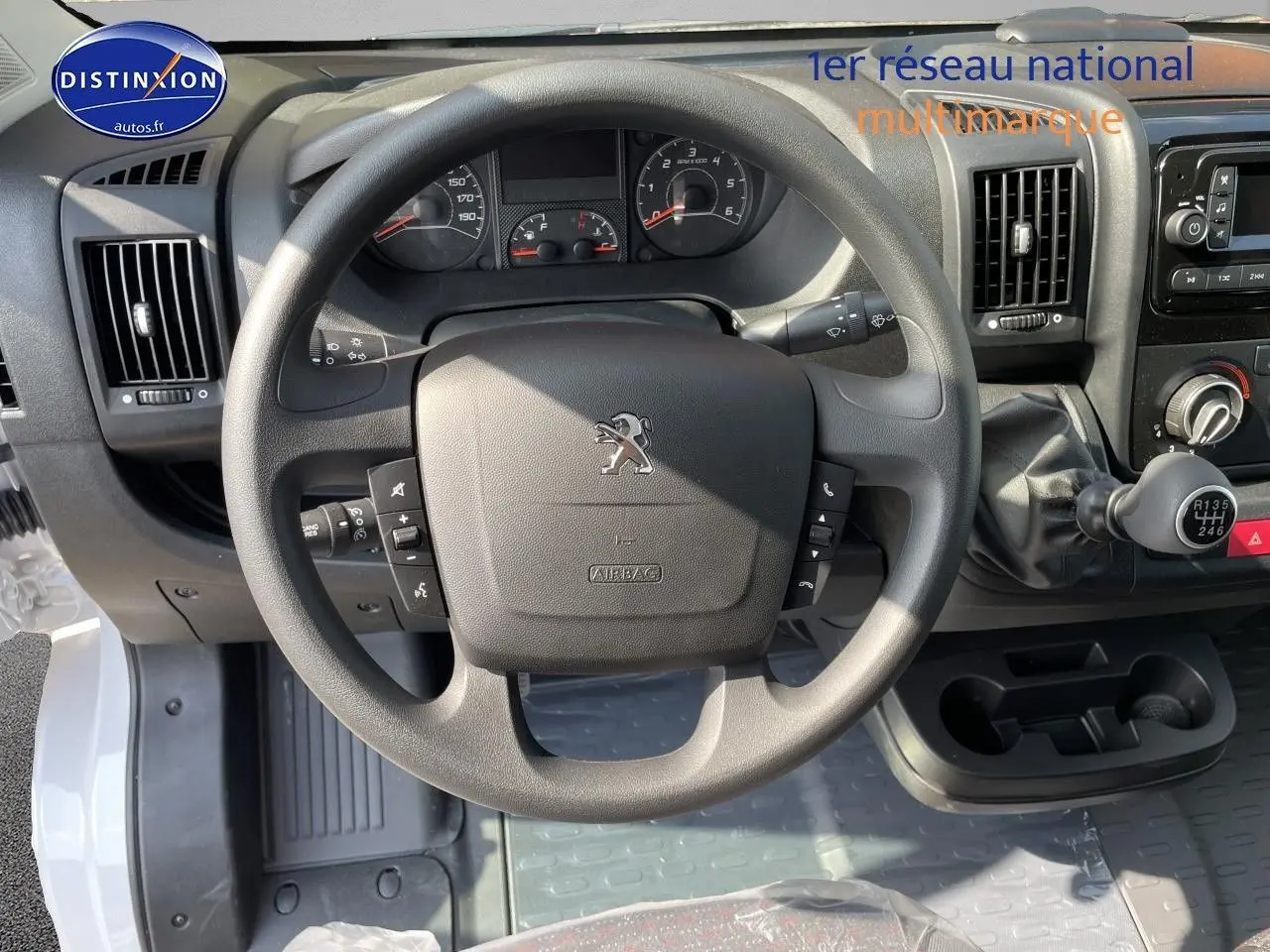 Vue intérieure centrée sur le volant noir du Peugeot Boxer Fourgon blanc, avec tableau de bord et levier de vitesses manuelle visibles.