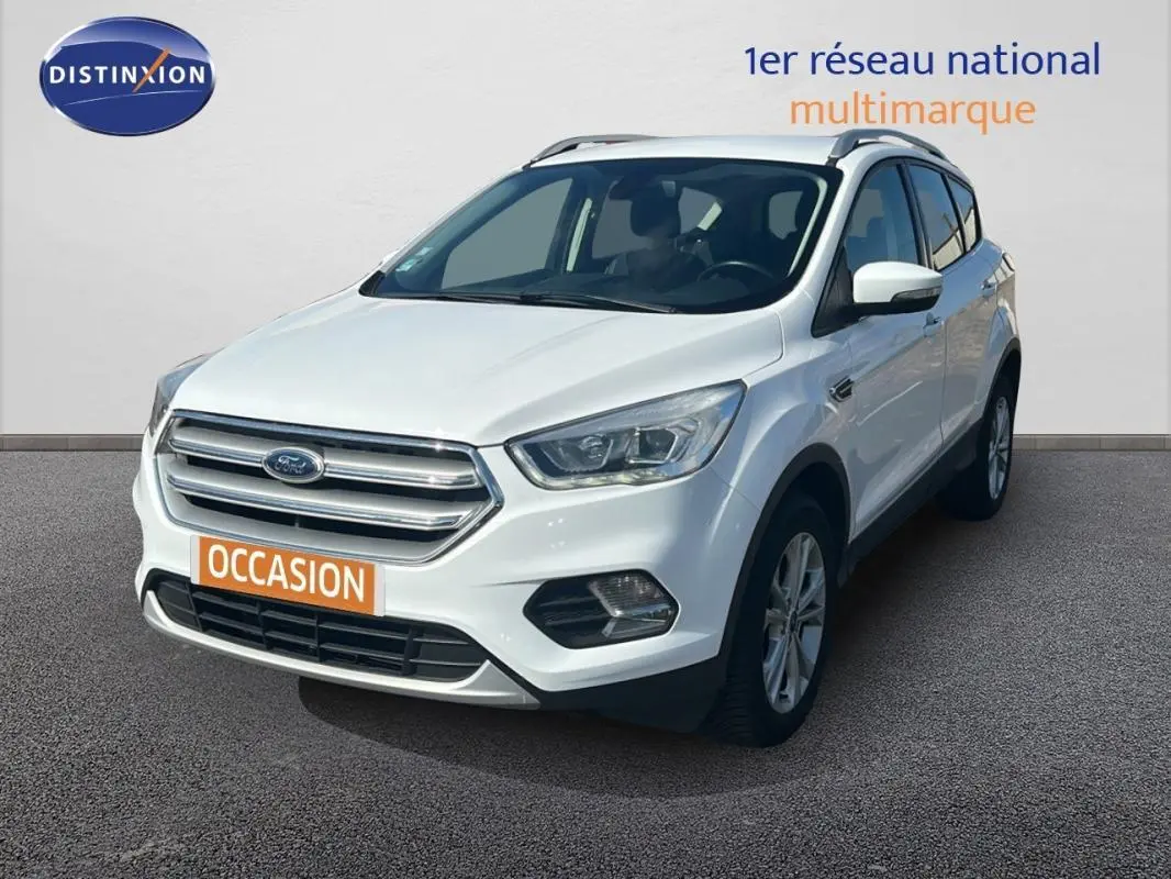 Ford Kuga blanc en 3/4 avant droit avec barres de toit et jantes alliage visibles sur sol gris.