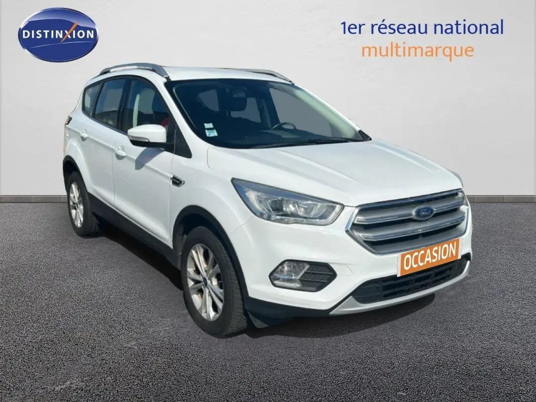 Ford Kuga blanc en 3/4 avant droit avec barres de toit et jantes alliage 17 pouces visible sur sol gris.