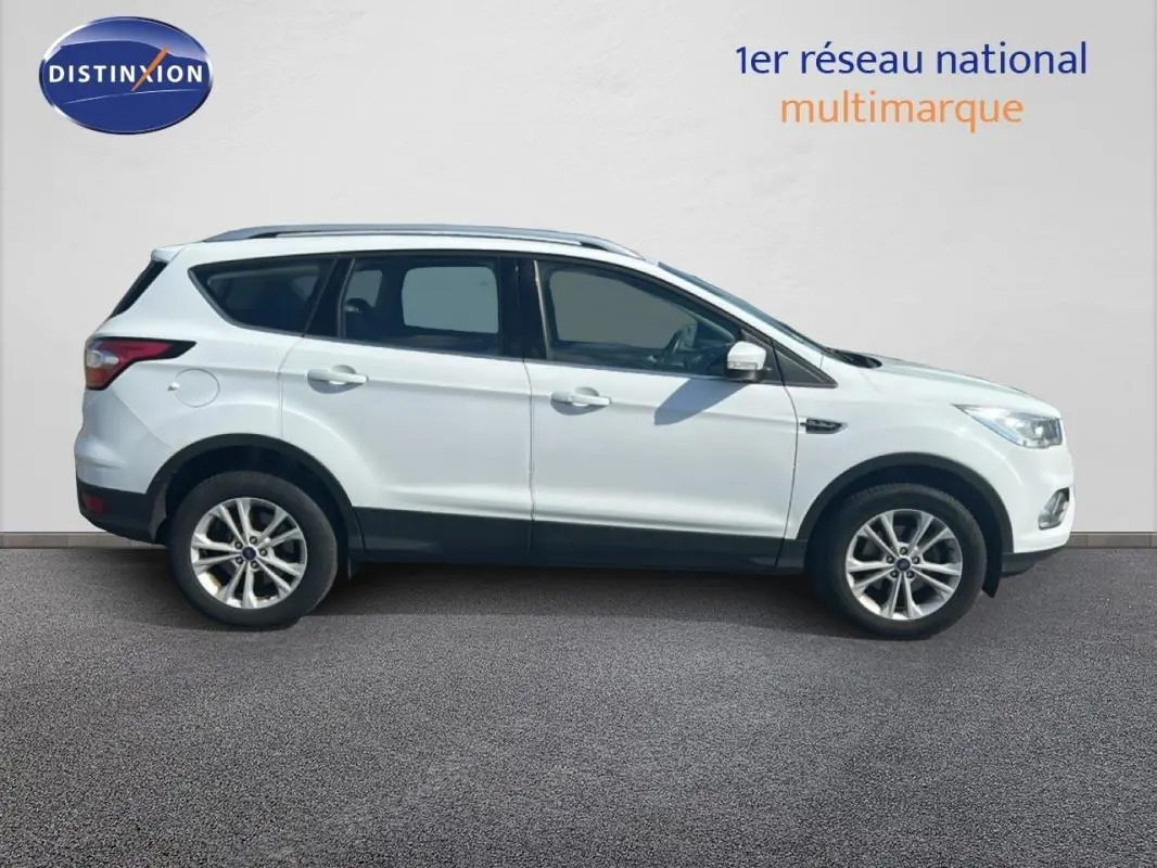 Ford Kuga blanc en profil droit, avec barres de toit et jantes alliage 17 pouces visibles.