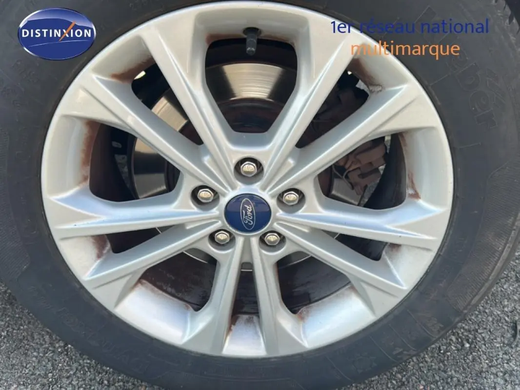Gros plan sur la jante alliage 17 pouces argentée d’un Ford Kuga blanc avec logo Ford au centre.