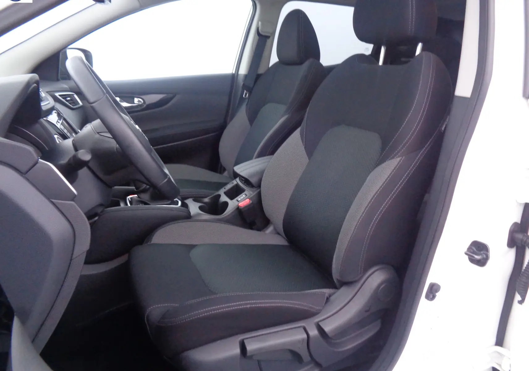 Vue intérieure côté conducteur du Nissan Qashqai blanc lunaire métal, sièges tissu noir et gris avec console centrale visible.