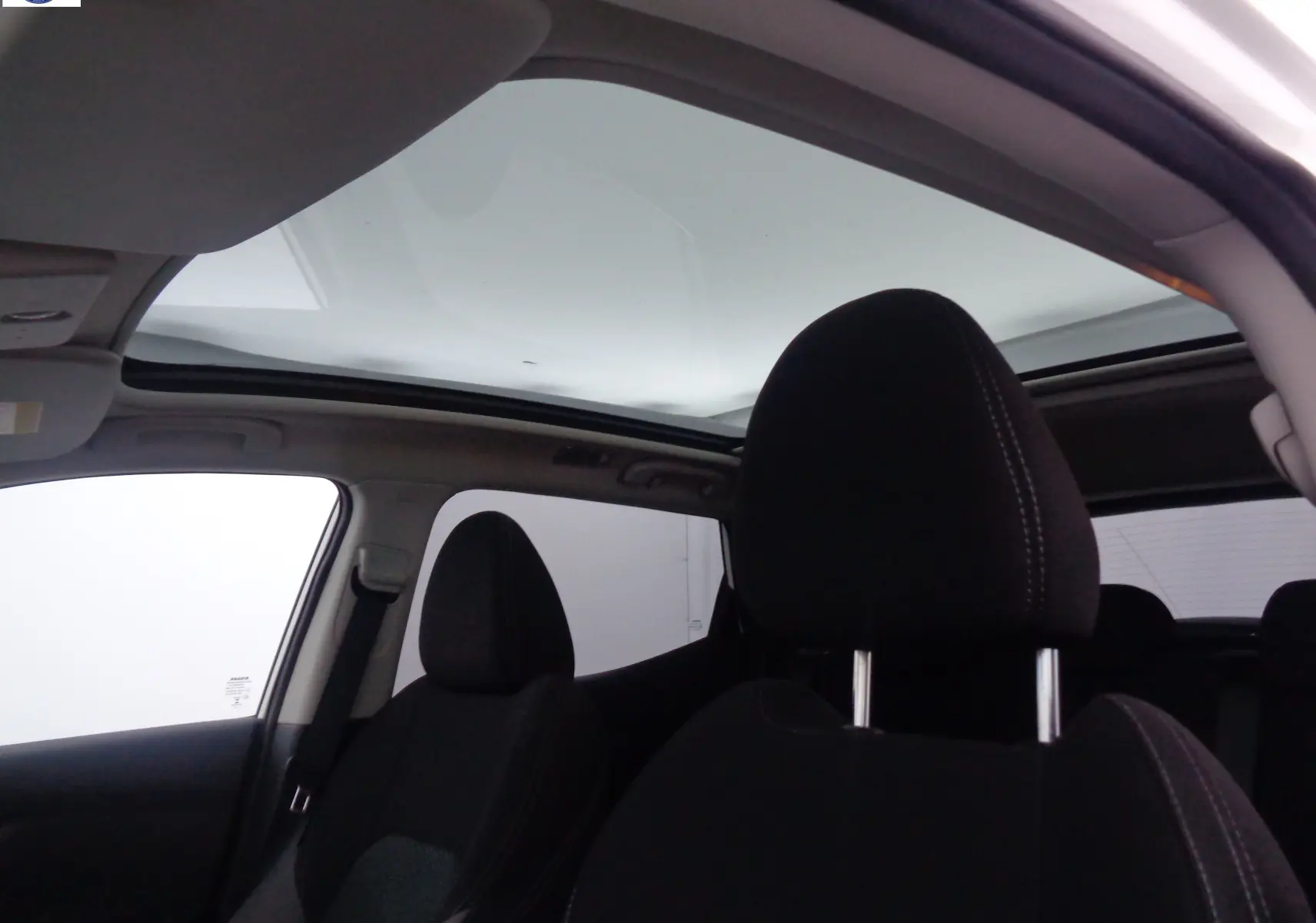Intérieur du Nissan Qashqai blanc lunaire, vue sur les sièges avant noirs et le toit panoramique vitré.