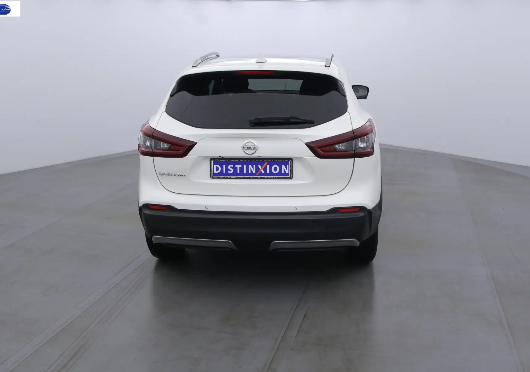 Vue arrière d'un Nissan Qashqai blanc lunaire avec feux arrière étirés et plaque Distinxion.