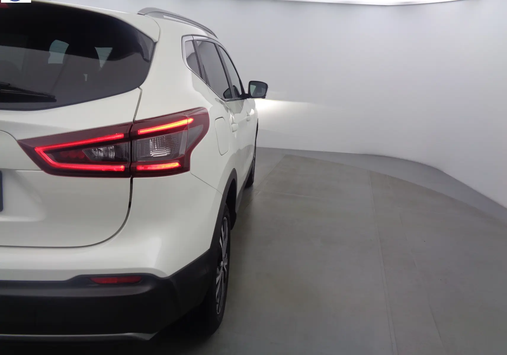 Vue 3/4 arrière droite du Nissan Qashqai blanc lunaire métal avec feux arrière allumés dans un studio.