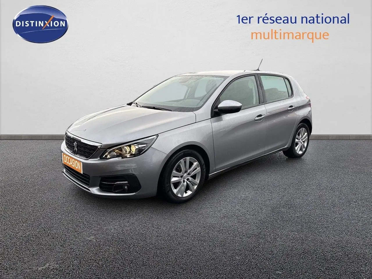 Peugeot 308 gris Artense vue 3/4 avant droit, compacte cinq portes avec phares allumés sur fond neutre.