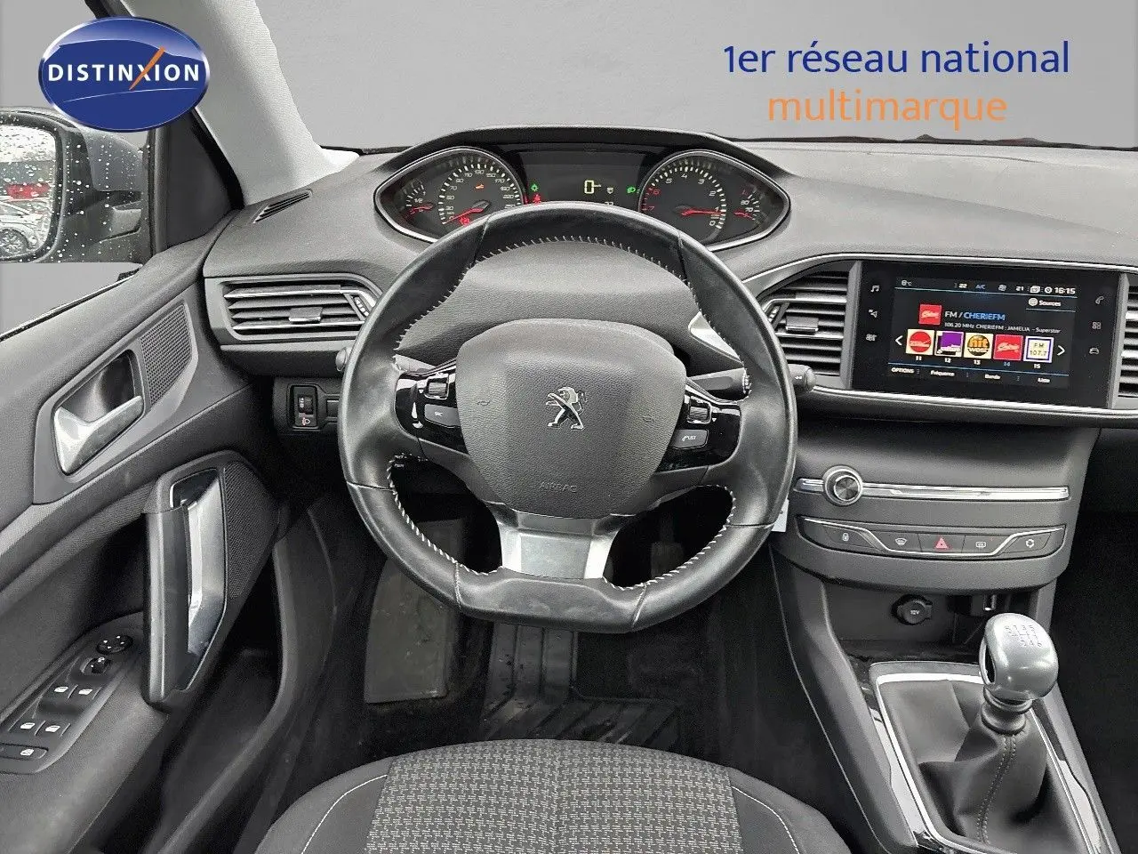Vue intérieure avant de la Peugeot 308 gris Artense de 2019, tableau de bord avec volant cuir et boîte manuelle visible.